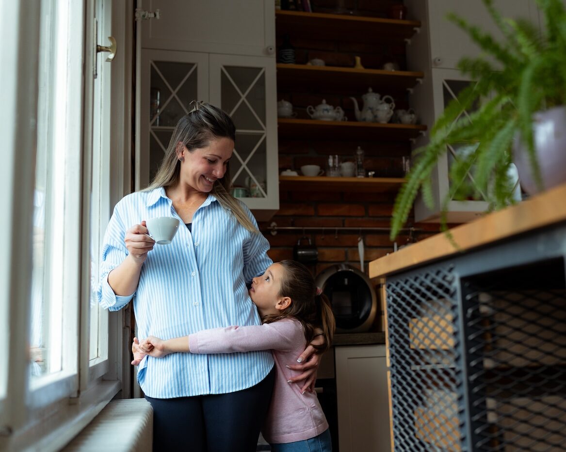 Mother enjoys a cup of coffee while her daughter hugs her affectionately in their modern kitchen