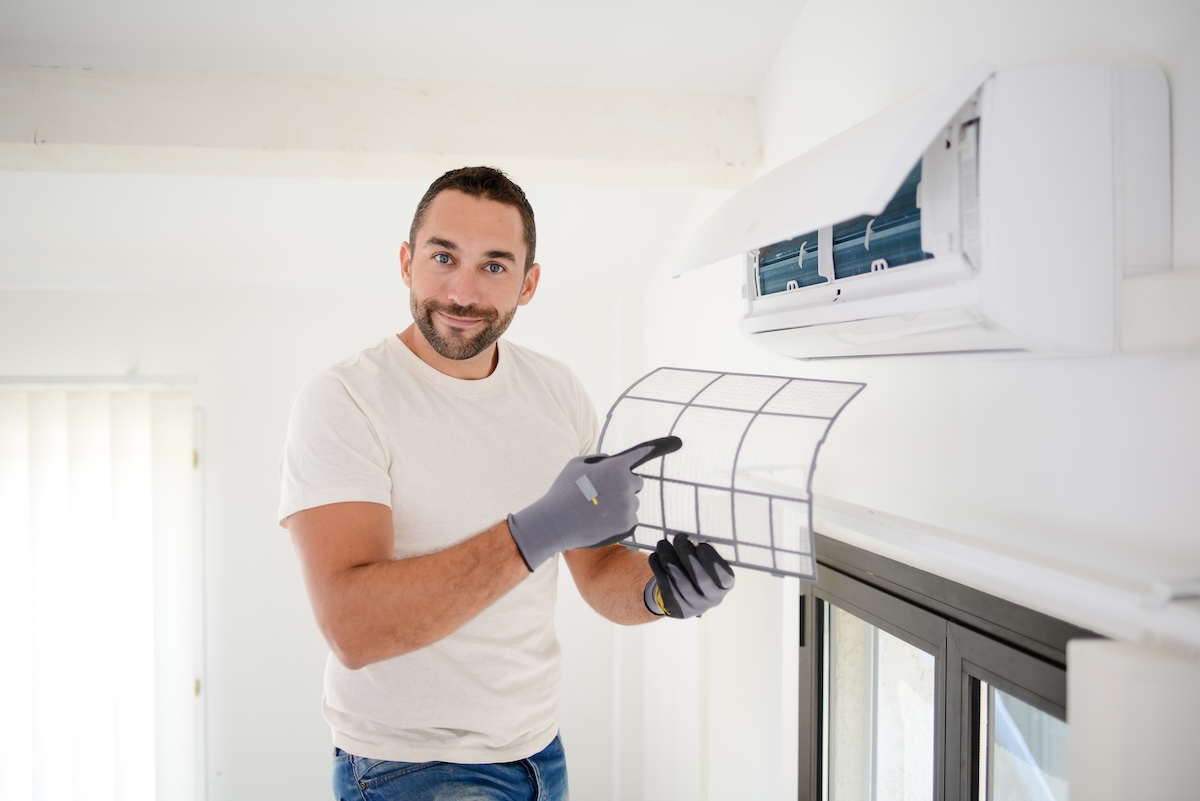 handsome young man electrician cleaning air filter on indoor unit of air conditioning in a client house