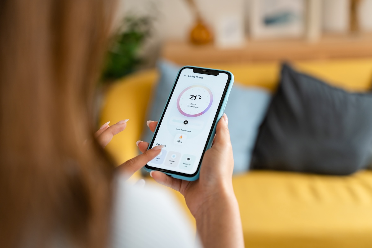 Woman controlling the temperature with a mobile phone, using modern technology to handle everything at home.