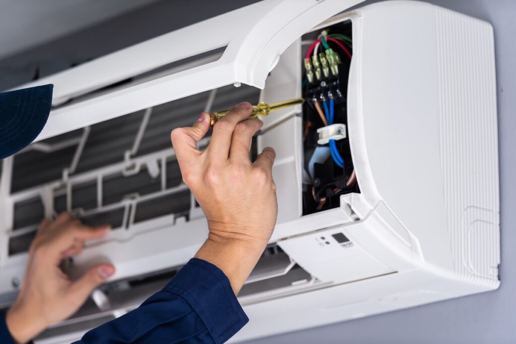 close up electrician with screwdriver repairing air conditioner indoors
